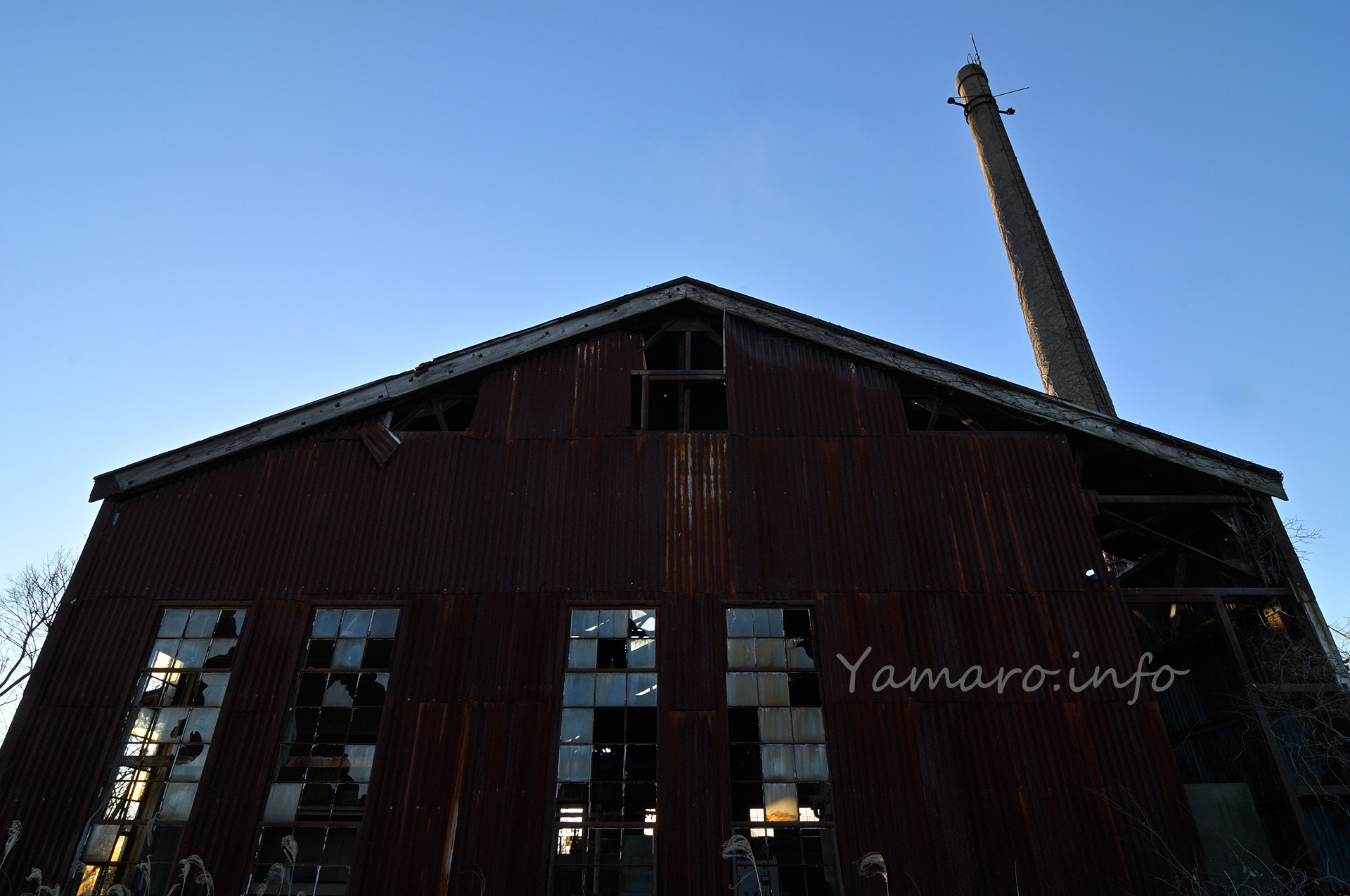 錆びついたトタンの壁、縦長の窓、破壊ではなく経年で割れたガラス。